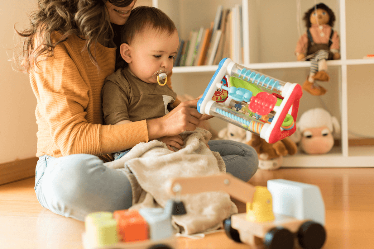 Mom with an infant playing with toys on the floor.