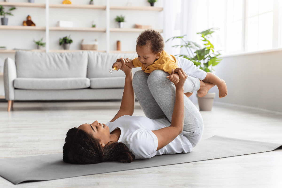 Young mom smiling and laying on the floor with infant on her legs playing