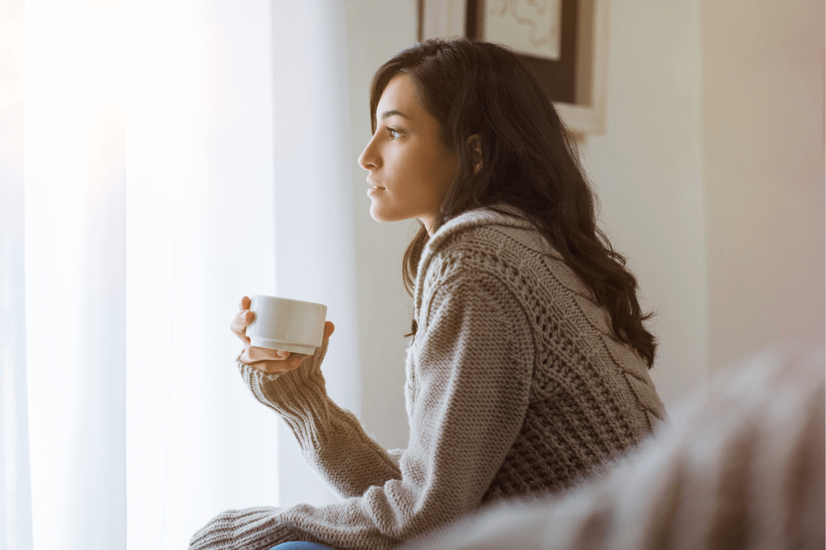 Young woman looking out a window thinking and holding a warm beverage