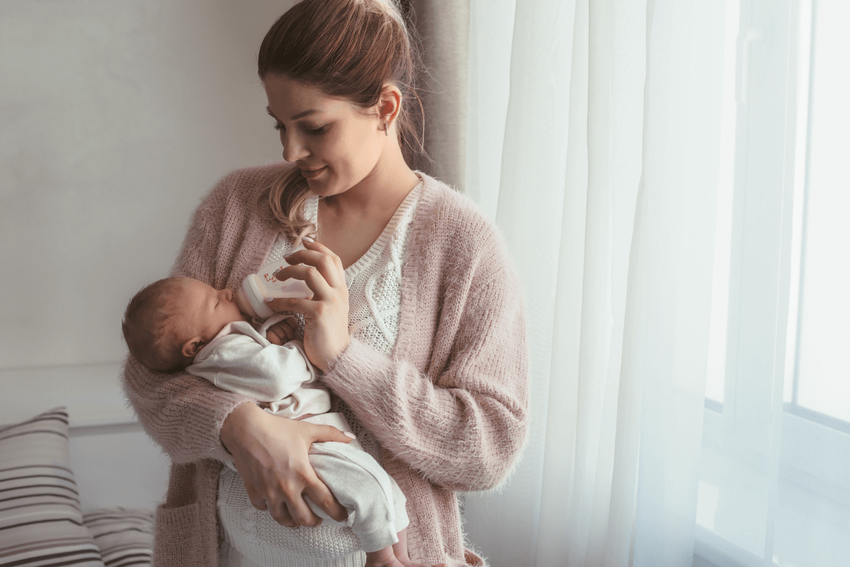 Young mom smiling while feeding infant in her arms a bottle